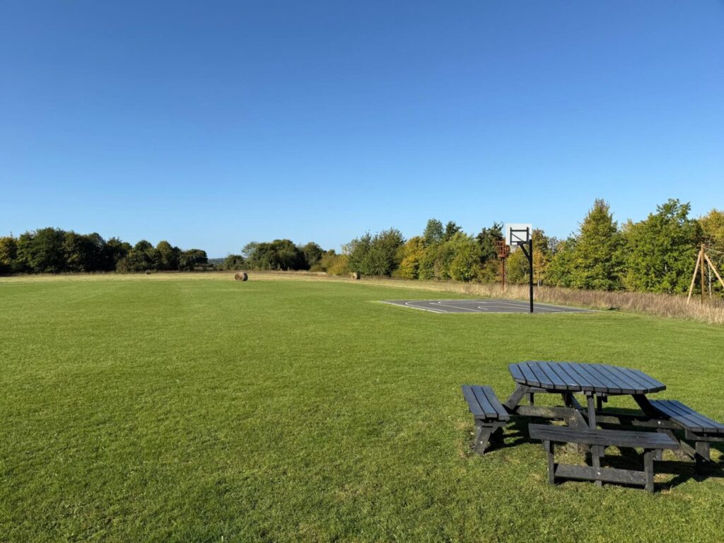 large field grass cutting with basketball court and a bench
